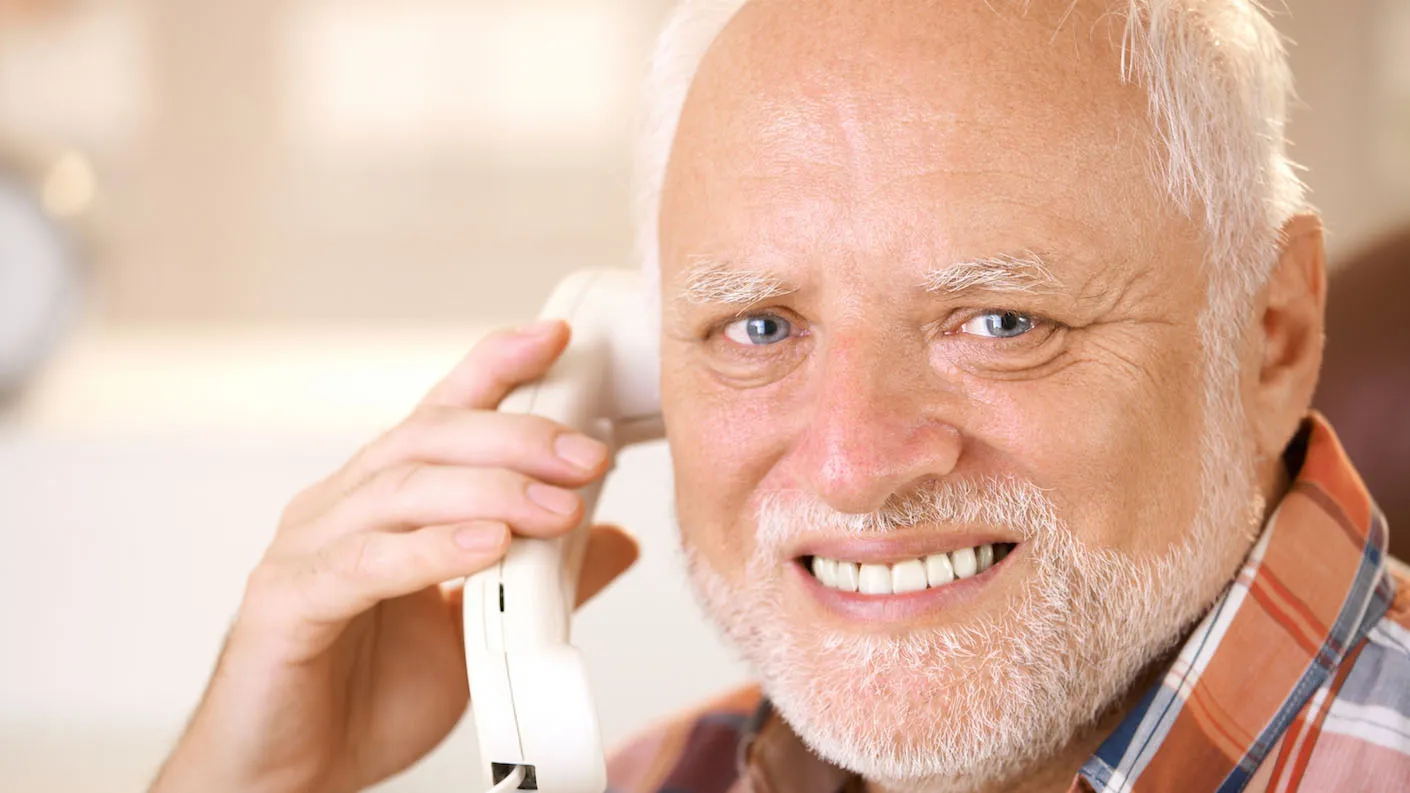 Meme do senhor de barba branca segurando o telefone e sorrindo com expressão de desconforto contido.